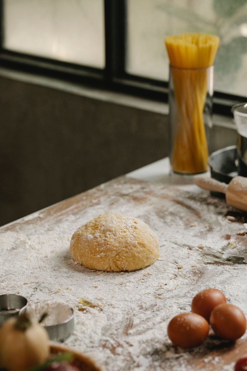 Fresh pizza dough being stretched with noodles beside it