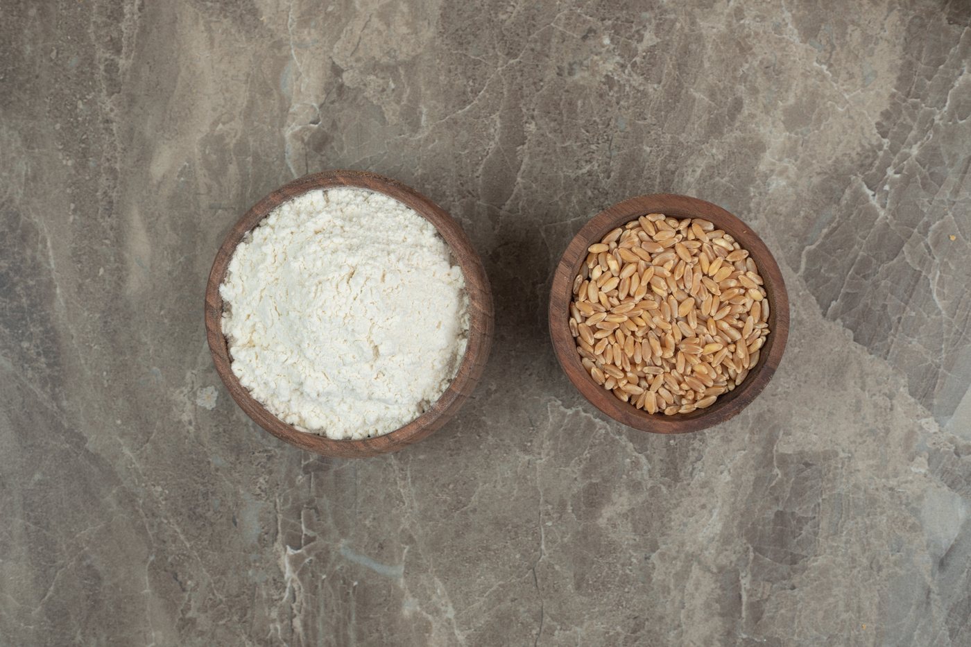Light creamy vital wheat gluten powder in a wooden bowl beside wheat heads